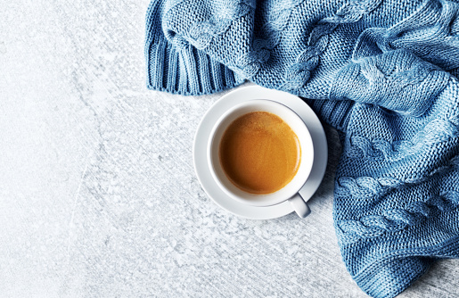 Cup of Coffee on gray background. A warm cloth beside the cup. Flat lay. Copy space