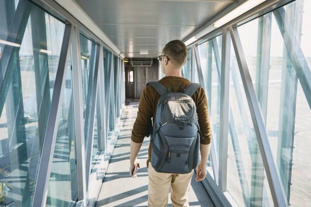 Boarding to airplane Traveling by airplane. Rear view of young man with backpack and passport in hand during boarding at airport. passenger boarding bridge stock pictures, royalty-free photos & images