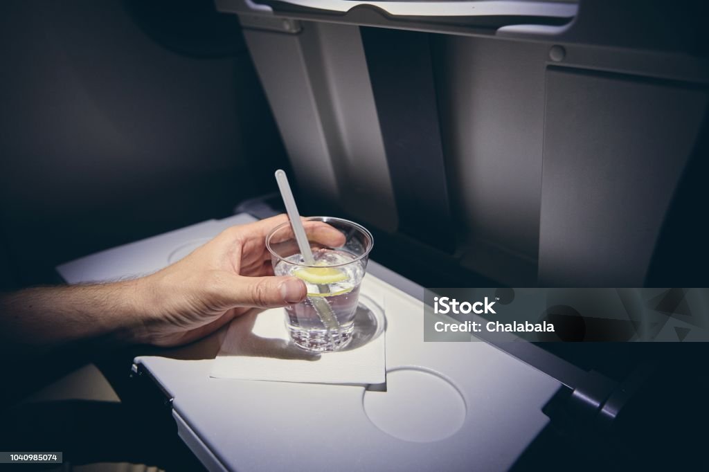Alcohol drink on board Traveling by airplane. Passenger enjoying gin and tonic drink in economy class during flight. Airplane Stock Photo