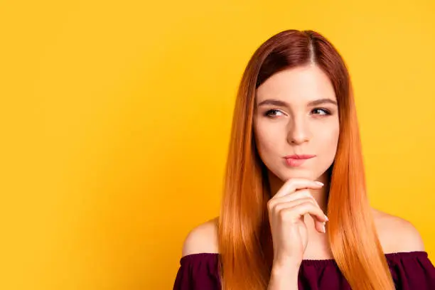 Photo of Portrait of red straight-haired attractive cute nice curious young girl, hand touching chin, thoughtful. Copy space. Isolated over bright vivid yellow background