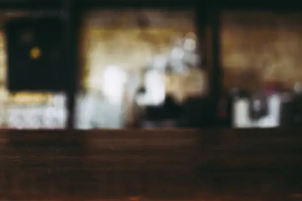 Photo of Blurred defocused interior of a craft beer pub. View from the vintage wooden counter. Bricked wall on the background. Popular place to drink with friends on Friday evenings.