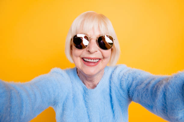 bouchent portrait de grand-mère heureuse prenant un selfie en vacances des deux mains, isolé sur fond jaune - senior women grandmother glasses senior adult photos et images de collection