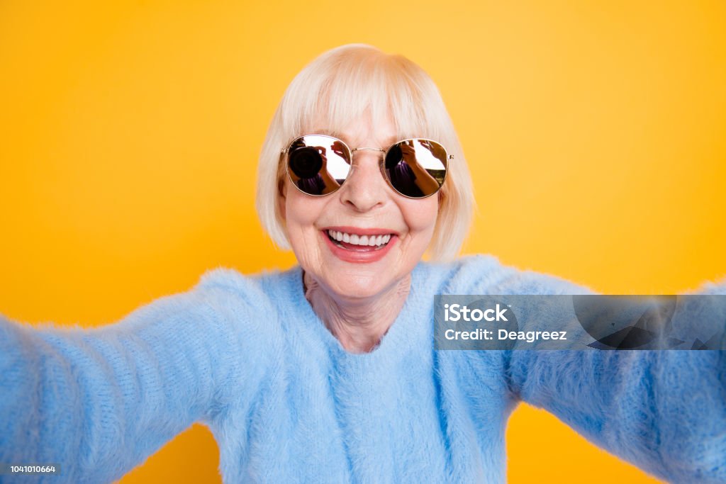 Close up portrait of happy grandma taking a selfie on vacation of two hands, isolated on yellow background Grandmother Stock Photo