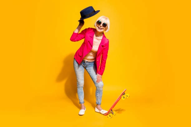 full-body full-legh portrait of happy granny with a board for skating isolated on vivid yellow background - shoe women retro revival fashion imagens e fotografias de stock