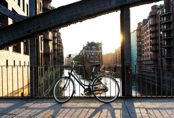 Photo of bicycle parked on bridge above water aganst Hamburg cityscape in evening sunlight