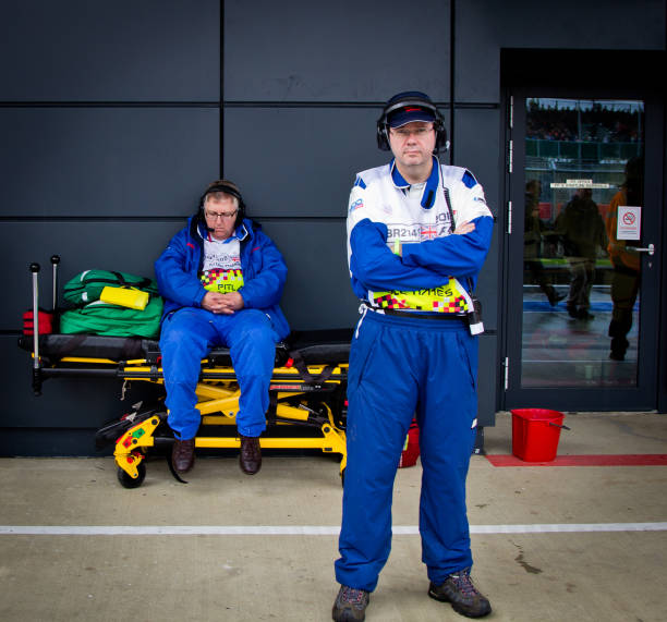 Two medical officials man a stretcher at an event. One is standing, while the other is asleep. Two medical officials man a stretcher at an event at Silverstone race track. One is standing while the other is sitting down, asleep, on the stretcher. silverstone stock pictures, royalty-free photos & images