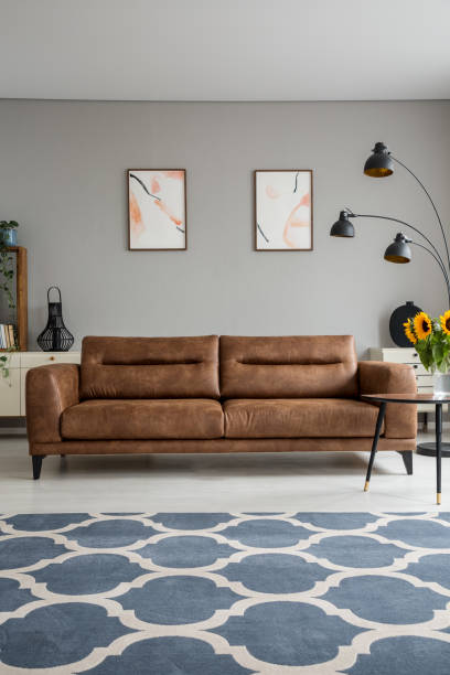 istock Blue patterned carpet and leather sofa in grey living room interior with posters and lamp. Real photo 1041019834