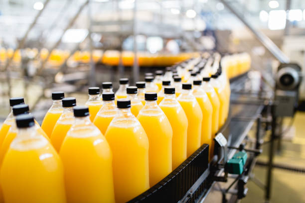 Bottling plant Bottling factory - Orange juice bottling line for processing and bottling juice into bottles. Selective focus. carbonated juice stock pictures, royalty-free photos & images
