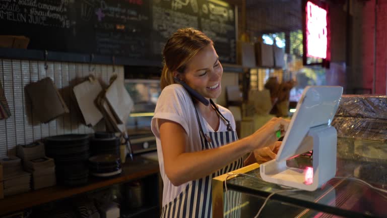 Beautiful young waitress registering a delivery on system while talking to customer on phone