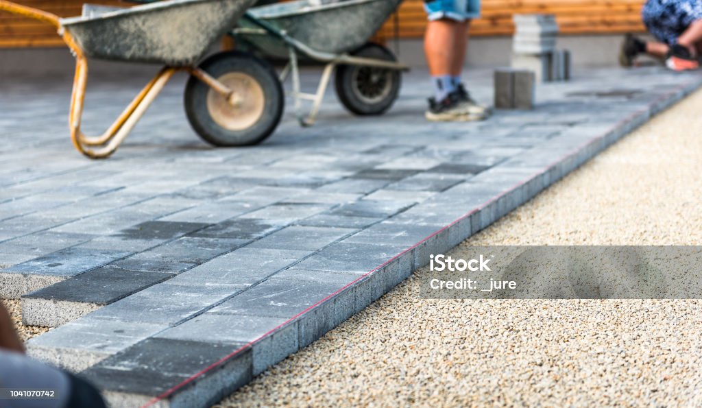 Laying gray concrete paving slabs in house courtyard driveway patio. Laying gray concrete paving slabs in house courtyard driveway patio. Professional workers bricklayers are installing new tiles or slabs for driveway, sidewalk or patio on leveled 
foundation base made of sand at public or private residence. Paving Stone Stock Photo