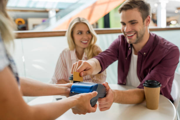 istock selective focus young man paying by credit card on terminal while his girlfriend sitting near at table with coffee cups in cafe 1041080768