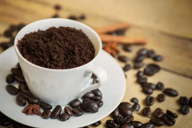 Ground coffee on the cup with coffee beans, anise, and cinnamon over wooden table, shot in the studio