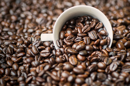 Macro shot of roasted coffee beans with a white coffee cup on the table, shot in the studio