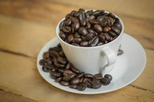 Closeup of roasted coffee beans on a cup and saucer over wooden table, shot in the studio