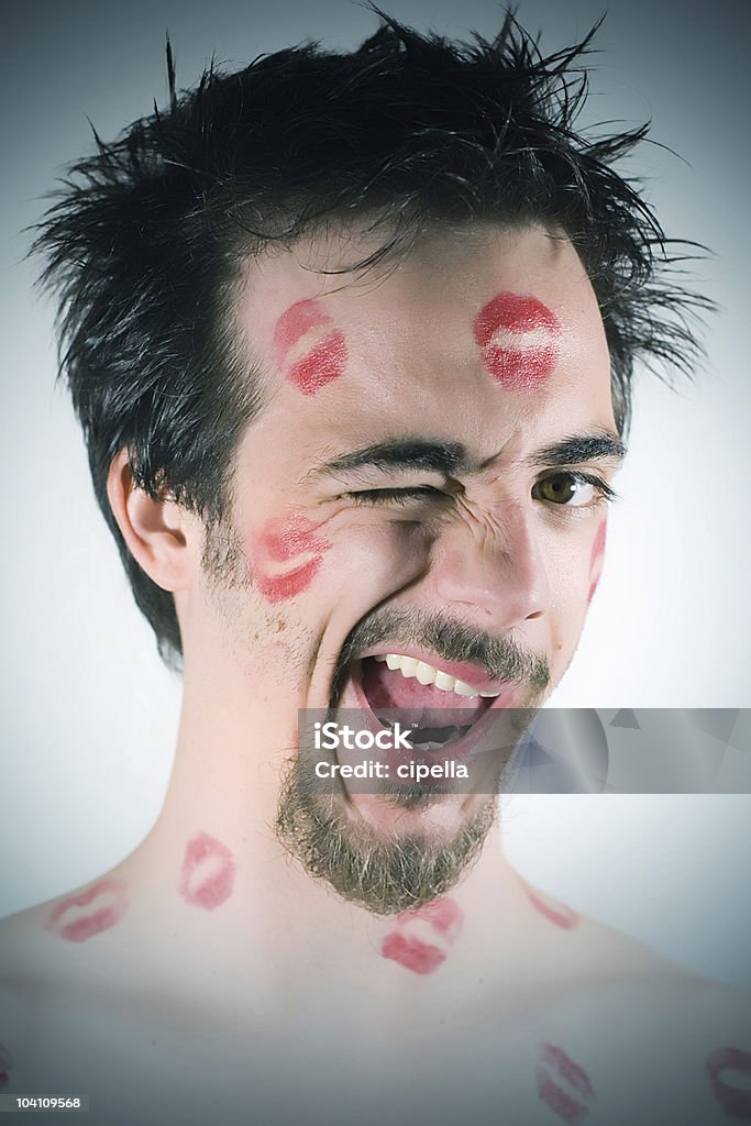 Close-up of man's face winking, covered in lip stick marks Young man with lipstick kisses all over his face. 25-29 Years Stock Photo