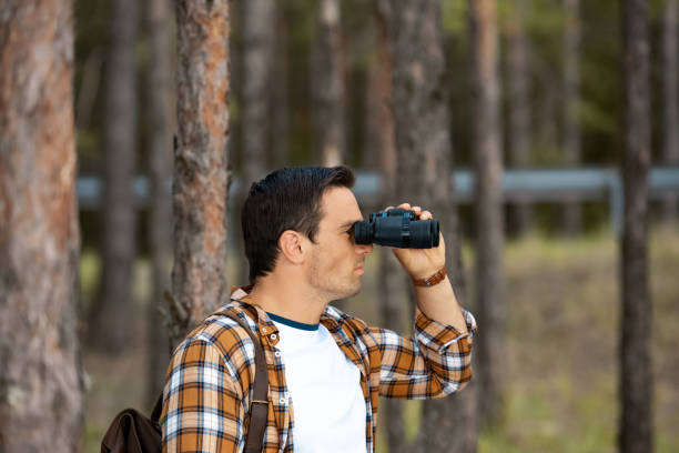 istock side view of tourist with backpack looking through binoculars in forest 1041096914