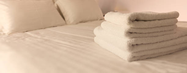 istock Hotel bedroom. White fluffy, folded towels, linen sheets and pillows on bed. Close up view. 1041097960