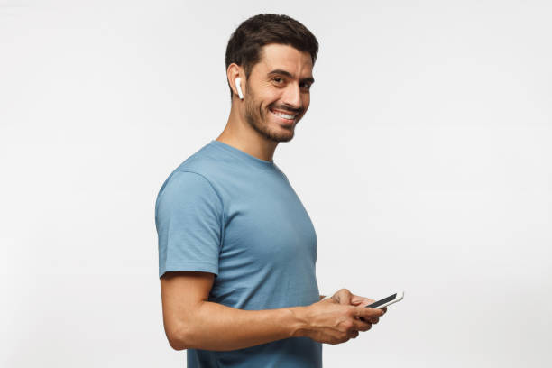 istock Young man looking and smiling at the camera with cheerful expression while texting to friend, using mobile phone, isolated on gray background 1041100876