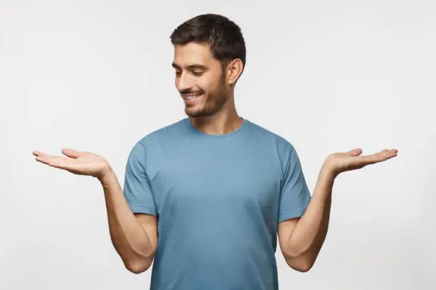 Photo of Choice concept. Portrait of young man choosing between 2 different options, holding two hands with empty space, isolated on gray background