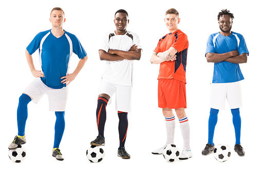 confident young multiethnic soccer players standing with balls and looking at camera isolated on white
