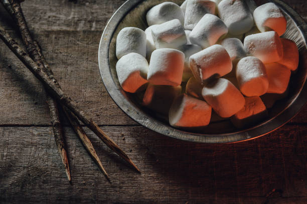 Bowl of marshmallows and skewers by fire light stock photo