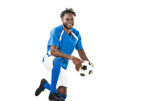 cheerful young african american soccer player holding ball and smiling at camera isolated on white