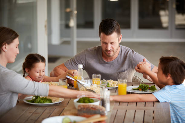 Show appreciation for what you have! Cropped shot of a family of four sitting down for a meal at home saying grace stock pictures, royalty-free photos & images