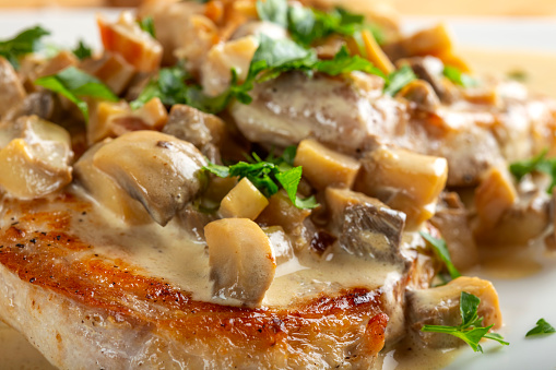 Fried pork meat with sour cream sauce, mushrooms and green parsley - close up view