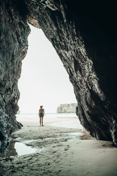 istock Woman standing on shore, seen from inside a cave in Asturias, Spain 1041125578