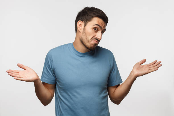 istock I don't know. Young man isolated on gray background, showing helpless gesture with arm and hands, mouth curved as if he does not know what to do 1041127062