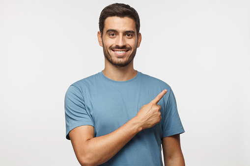 Young man in blue t-shirt pointing right with his finger isolated on gray background