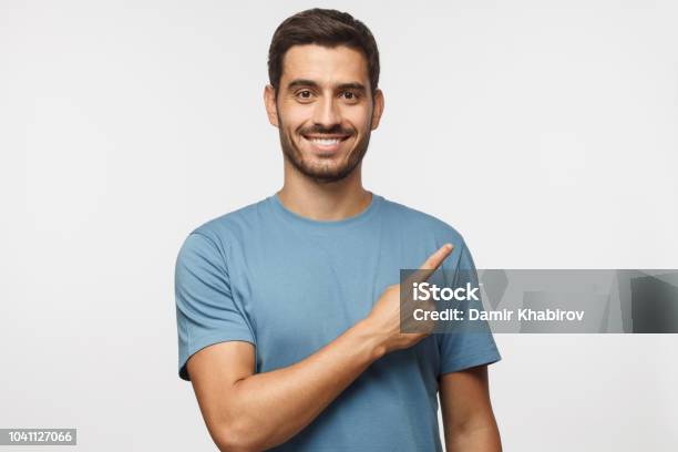 Young Man In Blue Tshirt Pointing Right With His Finger Isolated On Gray Background Stock Photo - Download Image Now