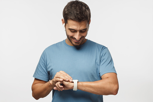 Young handsome man wearing wireless headphones and blue t shirt, checking smart watches with touch screen
