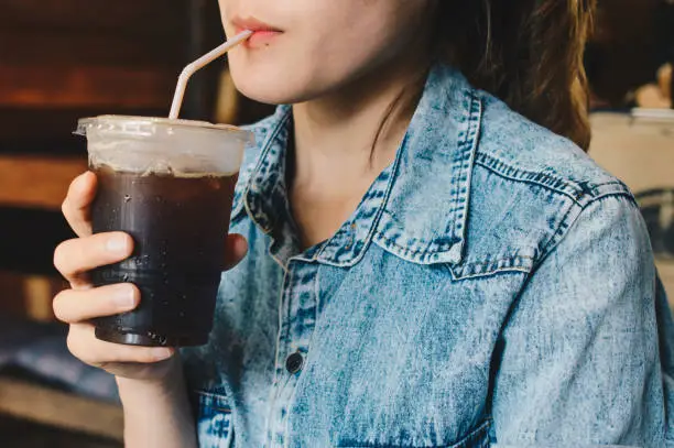 Photo of Cropped shot view of woman drinking Iced coffee/cold drink in the cafe.