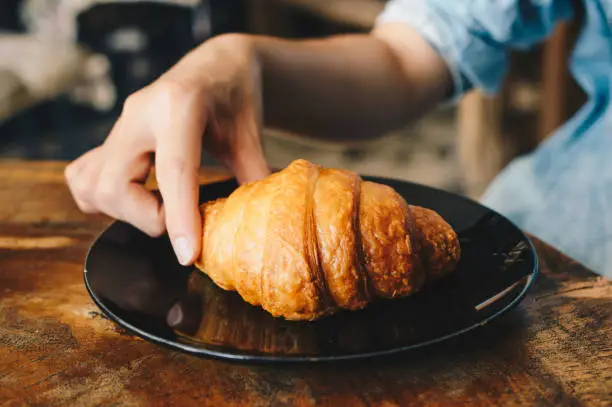 Photo of Cropped shot view of female hand catching croissant before eat.