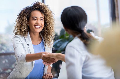 Attractive young mixed race businesswoman shakes hands with a female colleague during a business meeting.