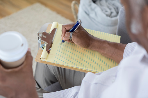 High angle view of unrecognizable African American man writing on a yellow note pad. He is also holding a coffee cup.