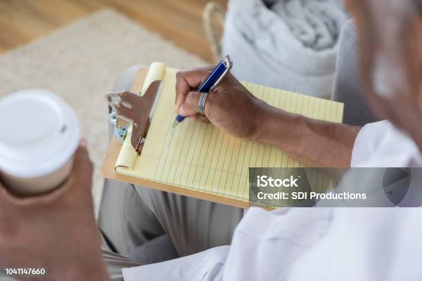 Unrecognizable Man Writes On Yellow Note Pad Stock Photo - Download Image Now - List, Writing - Activity, Senior Adult