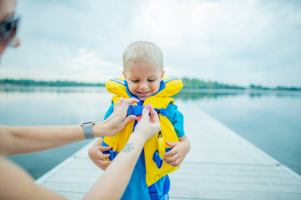 Helping Son With Life Jacket A mother is helping her son put on a life jacket. He is about to go swimming. life jackets stock pictures, royalty-free photos & images