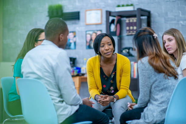 Group therapy session A diverse group of adults sit in a circle in their chairs and listen to and sympathize with each other with serious expressions. alcoholics anonymous photos stock pictures, royalty-free photos & images