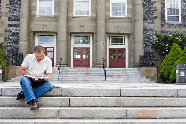 Man sitting on stairs reading a book stock photo