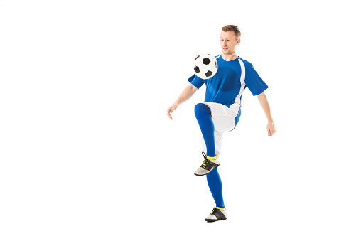 full length view of athletic young sportsman in soccer uniform training with ball isolated on white