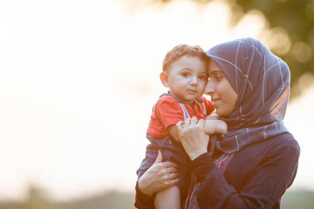 Cuddling Toddler A mother and young son are outdoors on a sunny day. The mother is lovingly holding her son in her arms. west asian ethnicity stock pictures, royalty-free photos & images