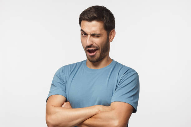 Studio shot of young man winking while flirting, isolated on gray background Studio shot of young man winking while flirting, isolated on gray background winking stock pictures, royalty-free photos & images