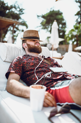 Tired Bearded Guy With A Straw Hat Sleeping and Listening Music At The Beach