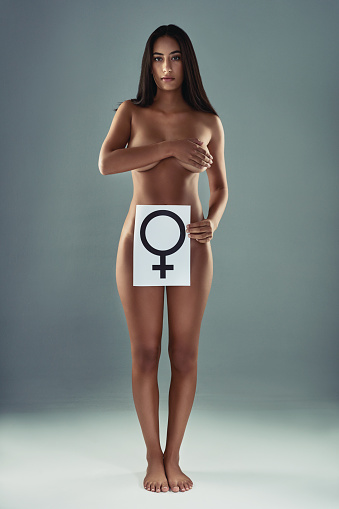 Studio shot of an attractive young woman posing and holding a poster with the female symbol on it against a grey background