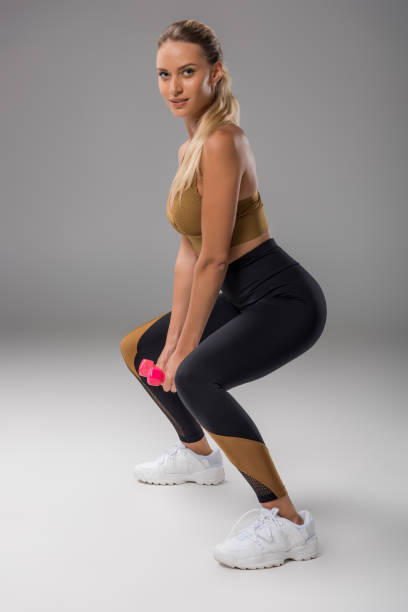istock sportive young woman doing squats with dumbbells on grey 1041218530