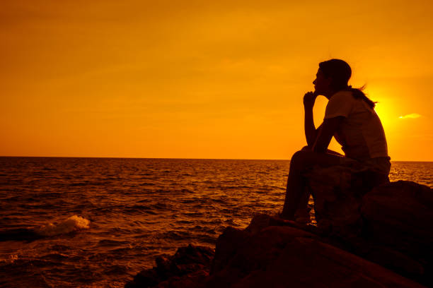 silhouette women sitting alone on the rock. mental health, ptsd and suicide prevention. - solicitous imagens e fotografias de stock