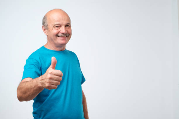 Everything is great. Positive nice mature joyful man in blue t-shirt smiling and showing thumb up sign stock photo