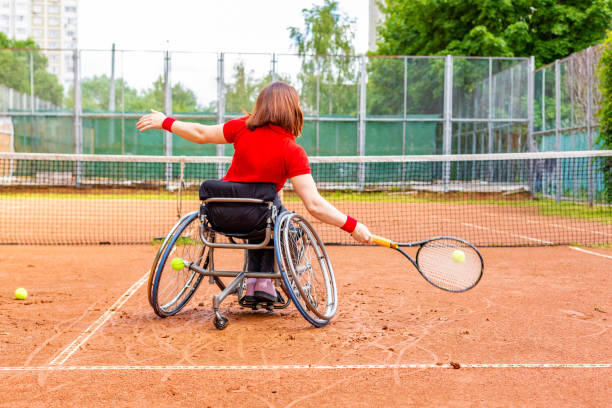Disabled young woman on wheelchair playing tennis on tennis court. stock photo
